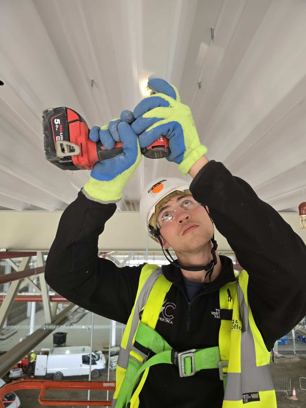 Electrician in PPE installing ceiling lighting on a commercial fit-out